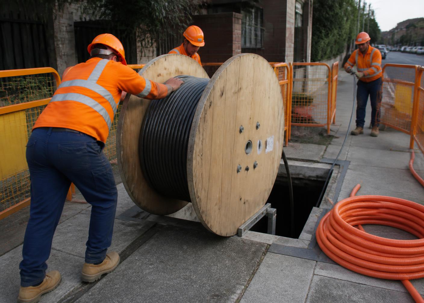 Workers hauling a fibre optic cable drum into a telecommunications pit
